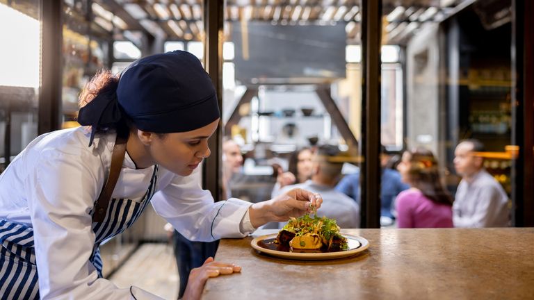 Female cook decorating a plate in the kitchen at a restaurant - food and drink establishment concepts